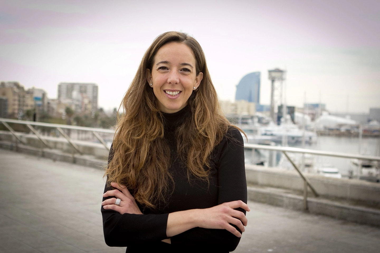 Carlota Pi lächelt in die Kamera. Sie steht auf einem Dach im schwarzen Rollkragenpullover. Im Hintergrund sieht man eine Stadt.