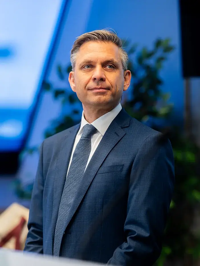 Wolfgang Hattmannsdorfer hat graumeliertes Haar. Er trägt ein weißes Hemd, eine mittelblaue Krawatte und ein dunkelblaues Sakko.