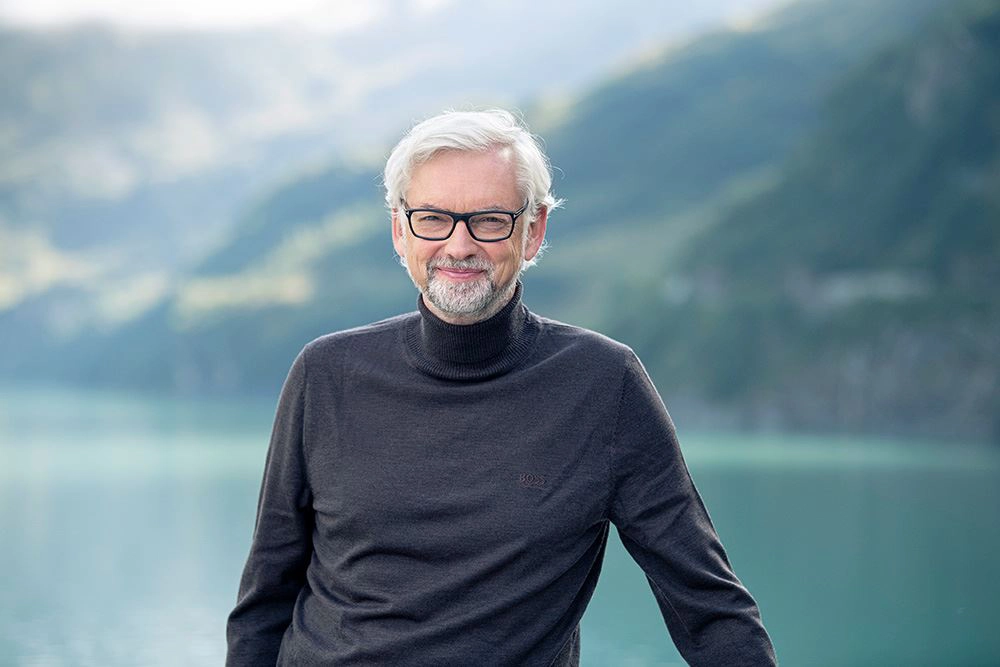 Michael Strugl lächelt in die Kamera. Im Hintergrund ein Stausee. Er trägt ein dunkelgrauen Rollkragenpullover.